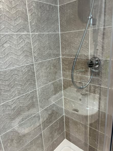 Clean grey chevron tiles and a chrome shower hose.